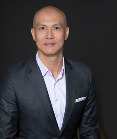 Eddie Koh in a suit and white shirt is smiling for a professional photo