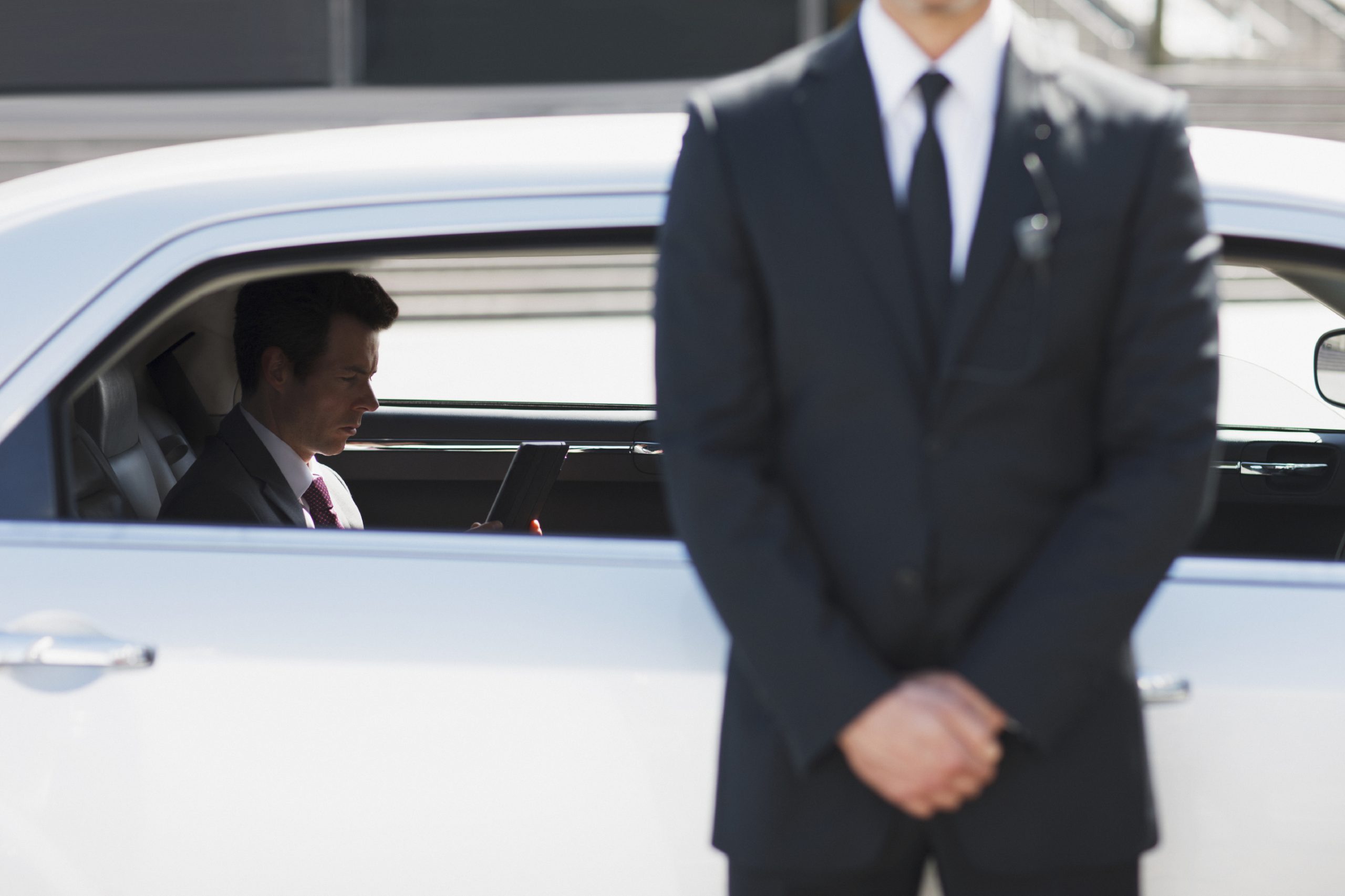 a male bodyguard in a suit and tie is standing next to a man in a white car