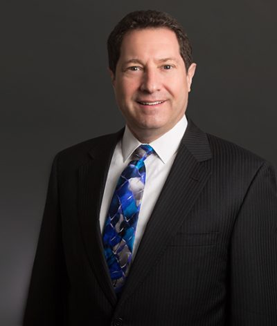 Ken Mendelson in a suit and tie smiling for a professional photograph