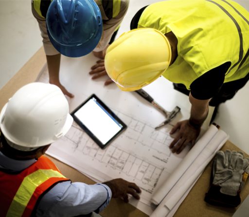 three construction workers are looking at a blueprint and a tablet