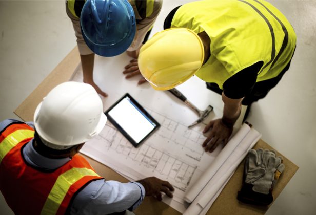 tres obreros de la construcción miran un plano y una tableta