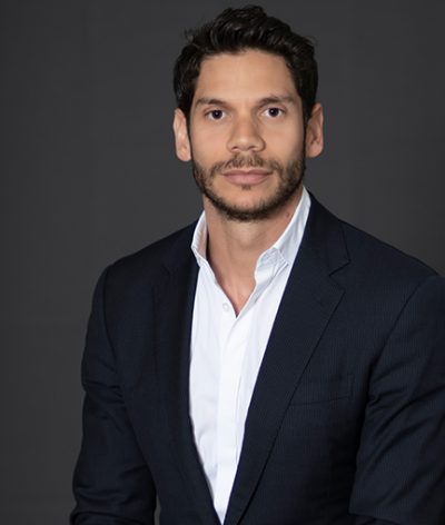 Yohir Akerman in a suit and white shirt is sitting in front of a black background