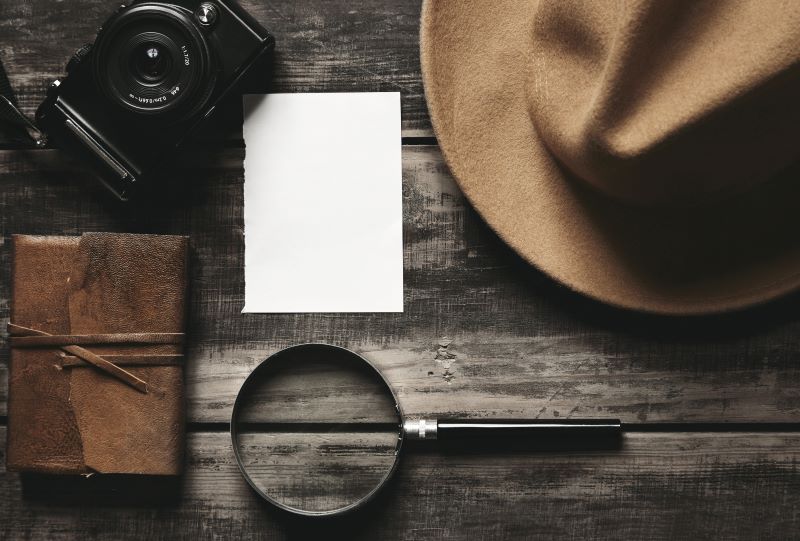 a hat, piece of paper, magnifying glass, and camera are on a wooden table