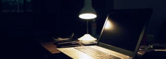 a laptop sits on a desk under a lamp in a dark room