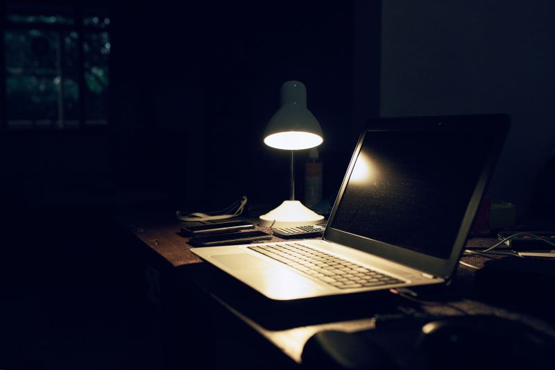 a laptop sits on a desk under a lamp in a dark room
