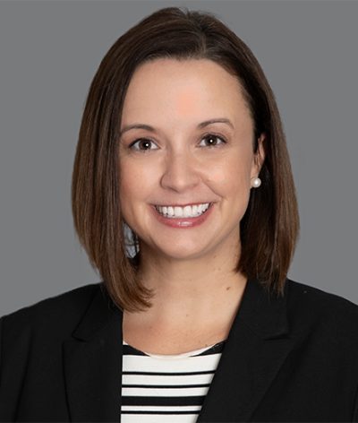 Sarah Pechnick wearing a black jacket and striped shirt is smiling for a professional headshot