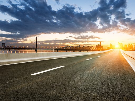 an empty highway with a city in the background at sunset